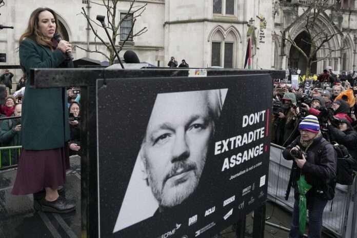 Stella Assange wife of Julian speaks besides a poster of J Assange at the Royal Courts of Justice in London