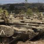An Israeli soldier sits on top of a tank at a staging ground