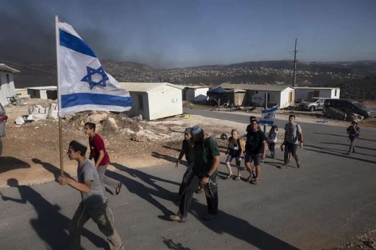 Israeli settlers carry an Israeli flag at the outpost of Eviatar near the northern West Bank town of Nablus 768x512 1